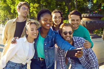 Multiethnic young happy people dressed in casual style smiling take collective selfie with friends on phone stands on city street on summer day. Inclusion, friendship of students concept