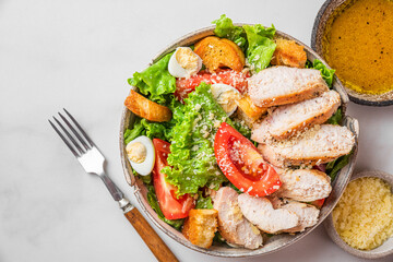 Wall Mural - Chicken salad. Caesar salad with chicken breast fillet in a plate with fork and dressing on white background. Top view