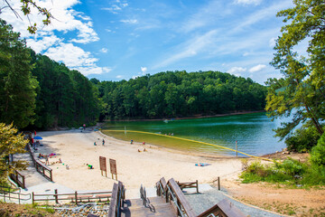 Wall Mural - a gorgeous summer landscape at the beach on green waters of Lake Allatoona with people in the water surrounded lush green trees, grass and plants with blue sky and clouds at Red Top Mountain park