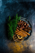 Overhead View Of A Plate With Hazelnuts, Cinnamon Sticks, Cloves, Star Anise, Dried Oranges And Thuja Branches
