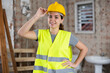Portrait of young female architect wearing yellow safety vest and helmet posing at construction site, looking at camera with smile