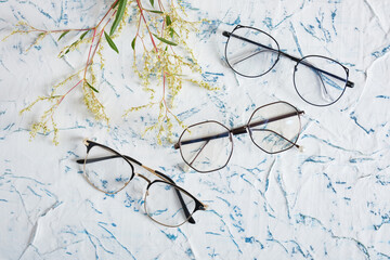 Canvas Print - Woman's eyeglasses and little yellow flowers branches on textured background. Flat lay