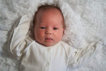 Wall Mural - A newborn baby in white clothes lies on a feather blanket looking at the camera