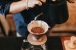 © sarayutsridee - Professional barista making filtered drip coffee in coffee shop. Close up of hands barista brewing a drip hot espresso coffee, pour over coffee with hot water and filter paper in coffee cafe.