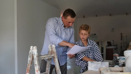 Wall Mural - Father and his young son discussing work plan in construction site in apartment, making pointing finger gesture.