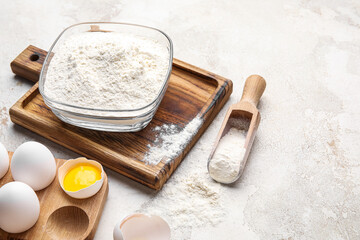 Wooden board with bowl of flour and chicken eggs on light background