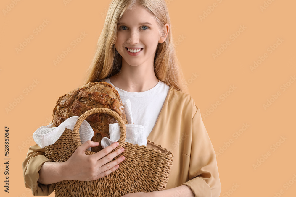 Young woman holding bag with fresh bread on beige background