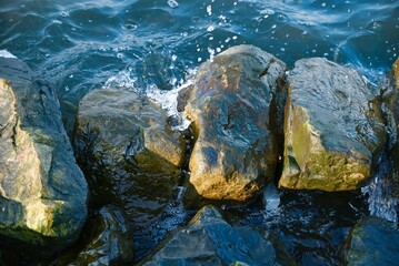 Sticker - Closeup shot of rocks getting hit by ocean waves on a coast in daylight