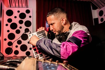 Closeup of a Hispanic DJ sitting near the table and controlling finger-drumming with headphones