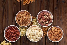 Top View Of Different Types Of Nuts Assorted In White Bowls On A Wooden Table