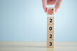 © tanoy1412 - 2023 new year challenge goal and target, Achievement and business success. Hand holding dartboard icon with stack of 2023 word on wooden blocks. Happy new year 2023. Business and financial concept.