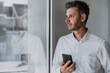 © Westend61 - Thoughtful businessman holding mobile phone looking through window