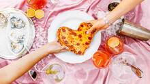 Hand's Of Women Pulling Heart Shaped Pizza At Table