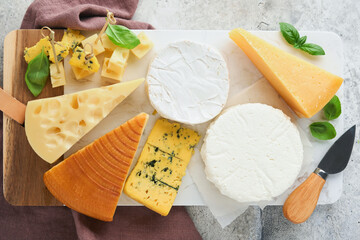 Set or assortment cheeses. Maasdam, smoked cheese, camembert, blue cheese, parmesan, brie cheese with basil and pepper on on white marble board white wooden old background. Top view. Free copy space.