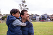 © Austockphoto - smiling middle aged man wearing blue sweatshirt carrying a smiling boy in his arms on a big lawn