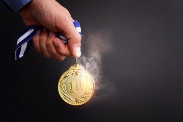 Wall Mural - male hand holding golden medal over dark background and light burst