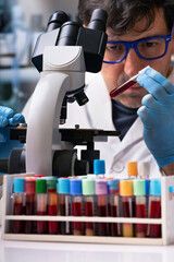 Wall Mural - Microscopist scientist analyzing blood sample in microscope in the microbiology laboratory. Hematologist with blood tube for examination on micro in the hematology lab