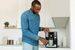 © Prostock-studio - Handsome young african american man using modern coffee machine in kitchen, making fresh aromatic coffee