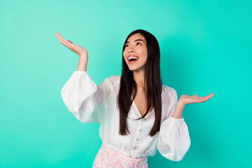 Wall Mural - Photo of positive pretty girl raise arms palms catch look empty space isolated on vivid aquamarine color background