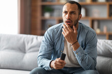 Shocked Black Man With Remote Controller In Hand Sitting On Couch