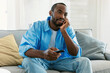 © Prostock-studio - Bored black man watching boring TV, switching channels holding remote controller, sitting on sofa at home