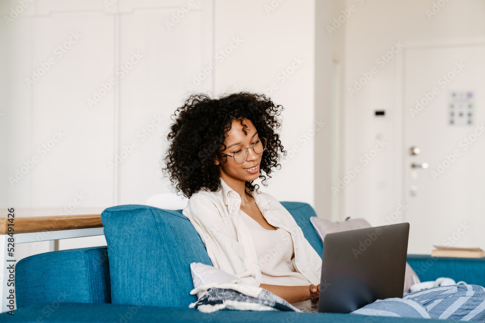 Black woman working with laptop while resting on couch at home Stock ...
