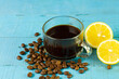Black coffee in transparent glass with fresh lemon and coffee bean on blue wooden background. Espresso romano drink for healthy.