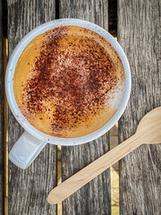 A freshly made mug of hot cappuccino with chocolate sprinkled on top on a wooden table. Closeup. Top view.