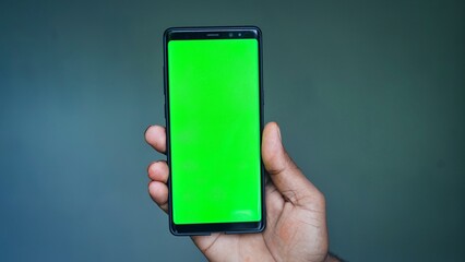 Indian man hand holding modern smartphone with green screen mockup on blue background.