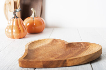 Wooden dish heart on light background. Serving, cooking, recipes for autumn dishes. Pumpkins in defocus.