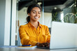 © Prostock-studio - Happy black businesswoman using laptop typing and working online while sitting at workplace in office, copy space