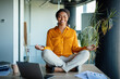Office zen. Calm black businesswoman meditating with closed eyes on office desk, sitting at workplace in lotus position