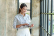 © amnaj - Beautiful Asian businesswoman standing and working on laptop with smiling face while working in office.