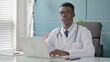 © stockbakers - Young African Doctor Looking at Camera while using Laptop in Office