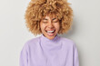 © wayhome.studio - Happy positive woman feels cheerful keeps eyes closed laughs gladfully smiles toothily dressed in casual purple pullover isolated over white background. People emotions and happiness concept