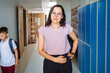 Portrait of positive friendly female teacher in eyeglasses at primary school at hallway.