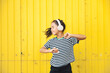 © inna717 - A child with headphones listening to music. Audiobook concept. Learning audio lessons. a little girl with headphones listening to music. a child is dancing on the background of a yellow fence