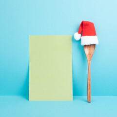 Blank paper with a wooden spoon and a red Santa Claus hat, christmas greeting card, copy space for a recipe for the holiday