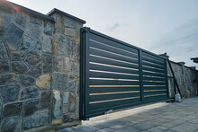 Wide Automatic Sliding Gate With Remote Control Installed In High Stone Fense Wall. Security And Protection Concept