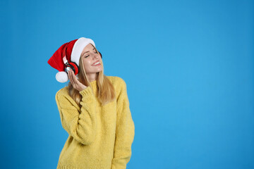 Wall Mural - Happy woman with headphones on blue background, space for text. Christmas music