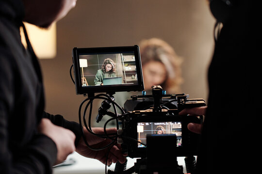 Close-up of steadicam screens with female model using laptop by table during commercial being shot by cameraman and his assistant