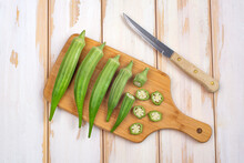 Green Okra Pods On Cutting Board With A Knife. On White Table.