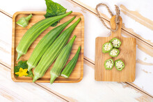 Green Okra Pods In  Wooden Bowl On A White Table.
