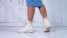 Unrecognized Woman In Blue Dress Shows The Light Leather Boots With Laces. New Fashionable Stylish Footwear At White Backdrop.