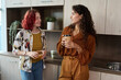 © pressmaster - Two young elegant female employees in smart casualwear having coffee and lunch while standing in the kitchen and chatting at break