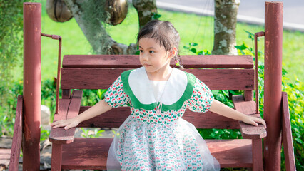 Wall Mural - Positive charming 4 years old cute baby Asian girl, little preschooler child sitting on swing chair and looking to the left