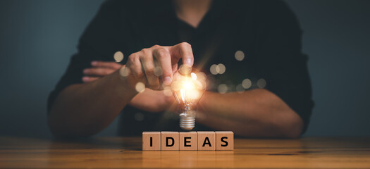 Aufkleber - hand touching on light bulb on wood block with Word Ideas, new idea concept with innovation and inspiration, innovative technology in science and communication concept...