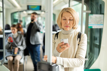 Portrait of focused mature woman absorbed in her smartphone on way to work in modern streetcar in autumn day