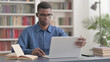 © stockbakers - Young African Man Coming Back Opening Laptop in Office
