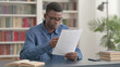 © stockbakers - Young African Man Reading Documents in Office
